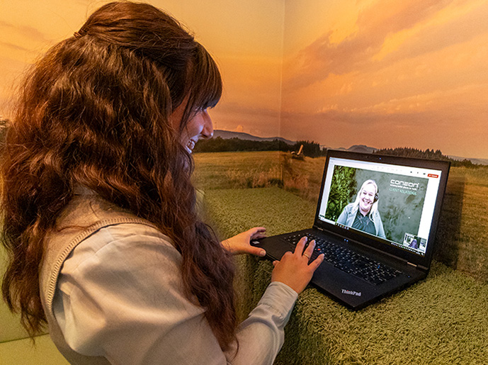 Eine Frau steht vor ihrem Laptop und hält einen Videocall mit einer anderen Person