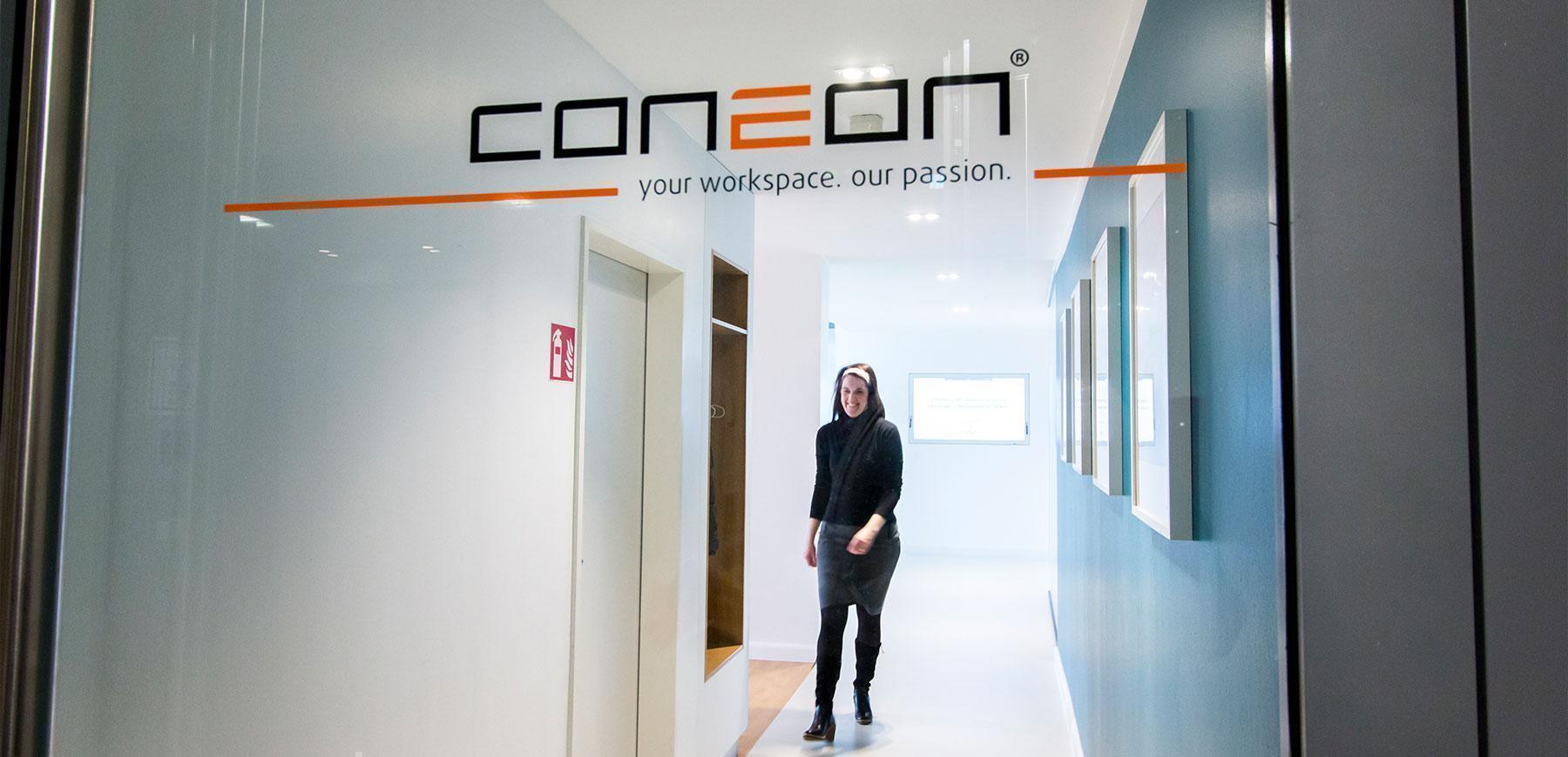 Das Coneon-Logo auf einer Glasscheibe mit einer Person, die im Hintergrund geht und lächelt.